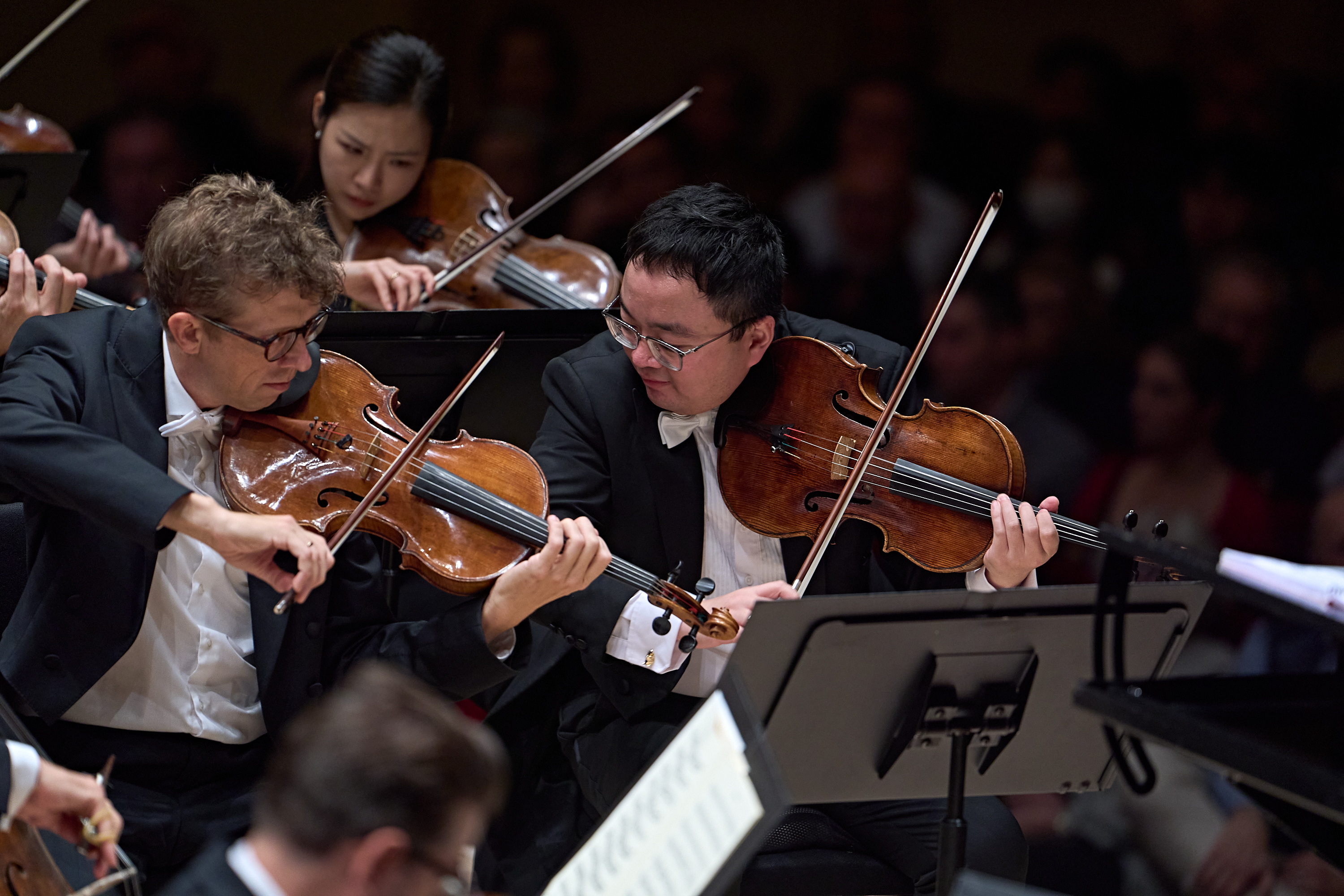 Zwei Bratschisten in Konzertkleidung, die sich während eines Orchesterkonzerts lächelnd ansehen.