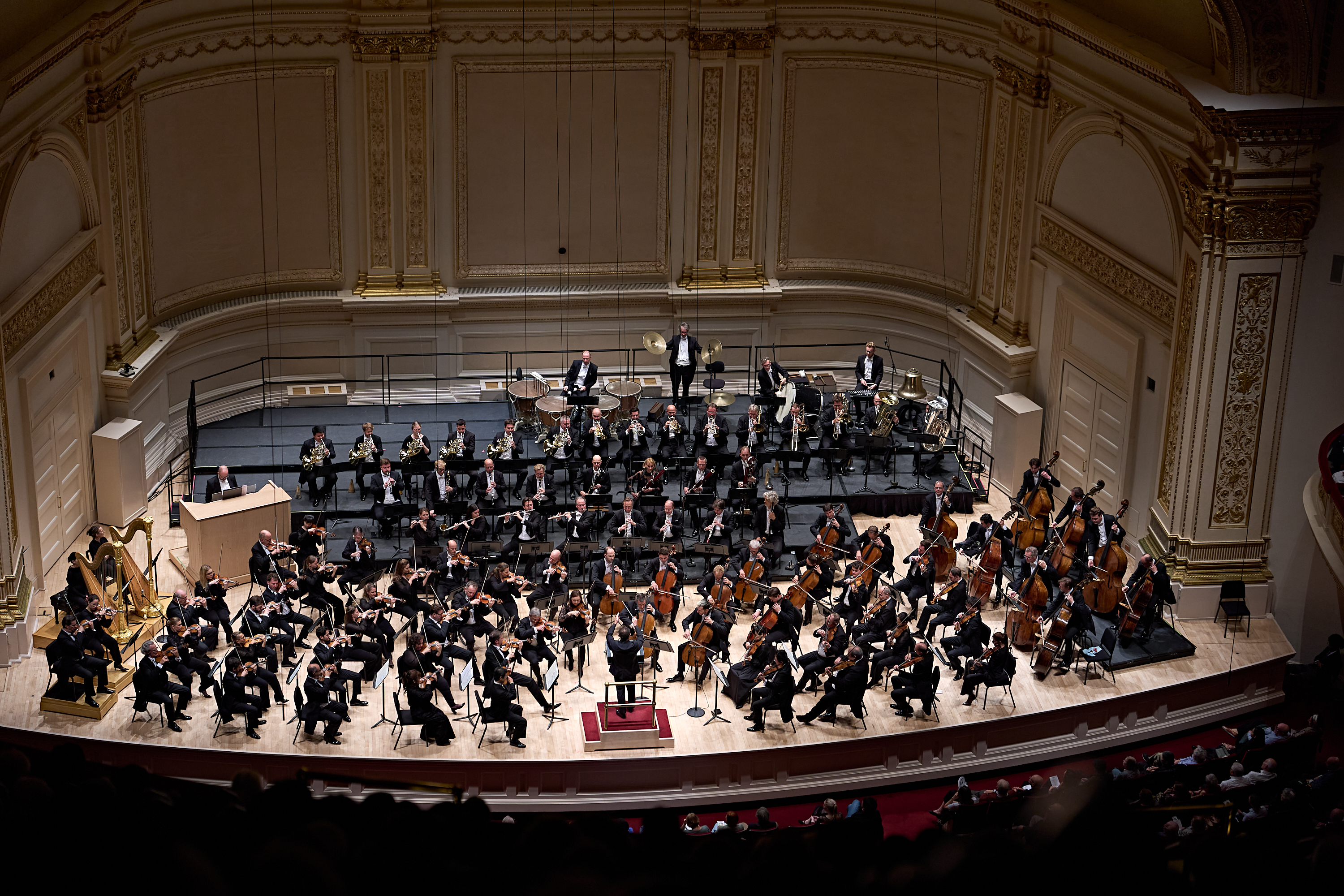 Ein Sinfonieorchester, das auf der Bühne eines prunkvollen Konzertsaals auftritt, von oben gesehen.