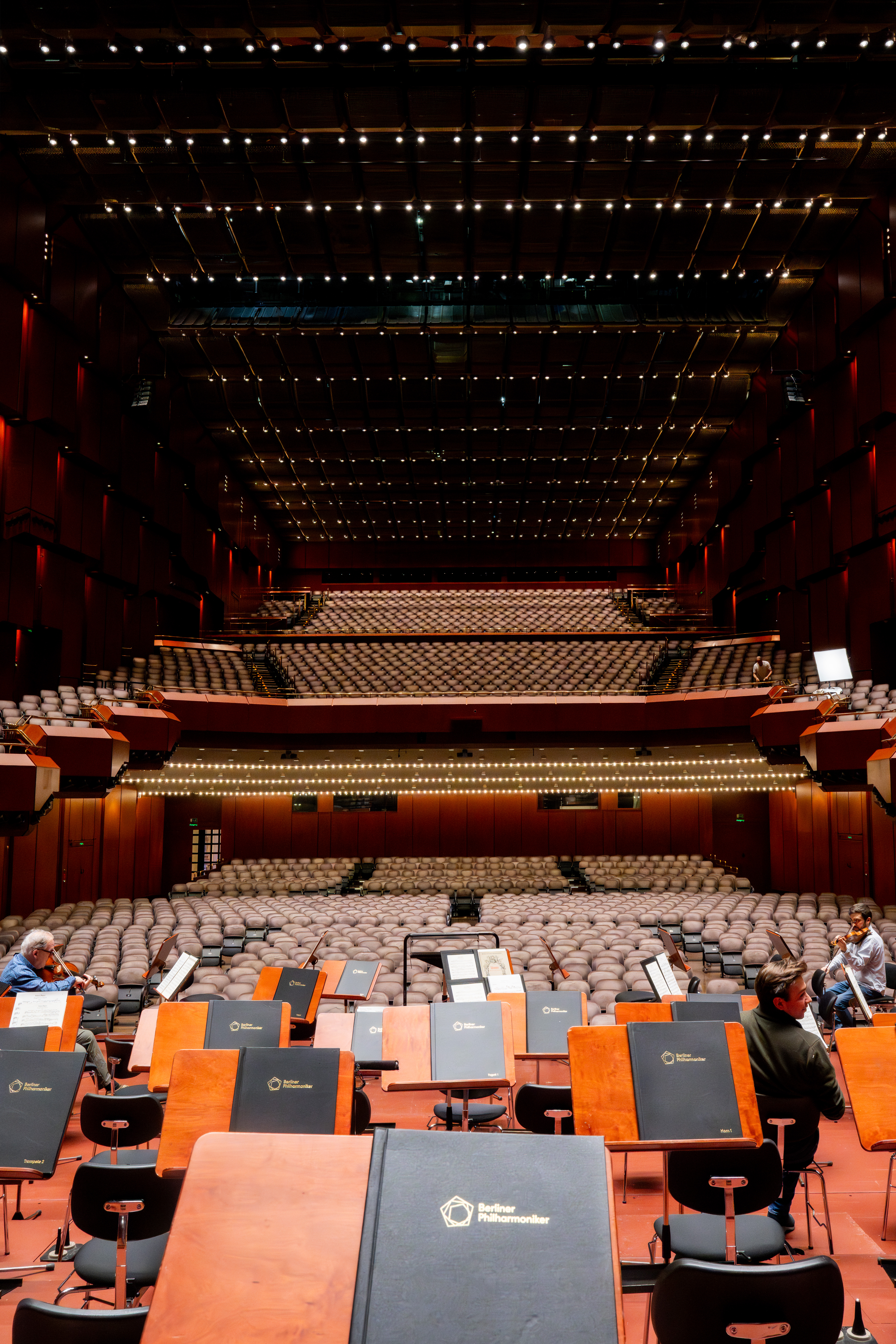 View from the stage into the warmly lit concert hall with music stands and a few people preparing for the performance.