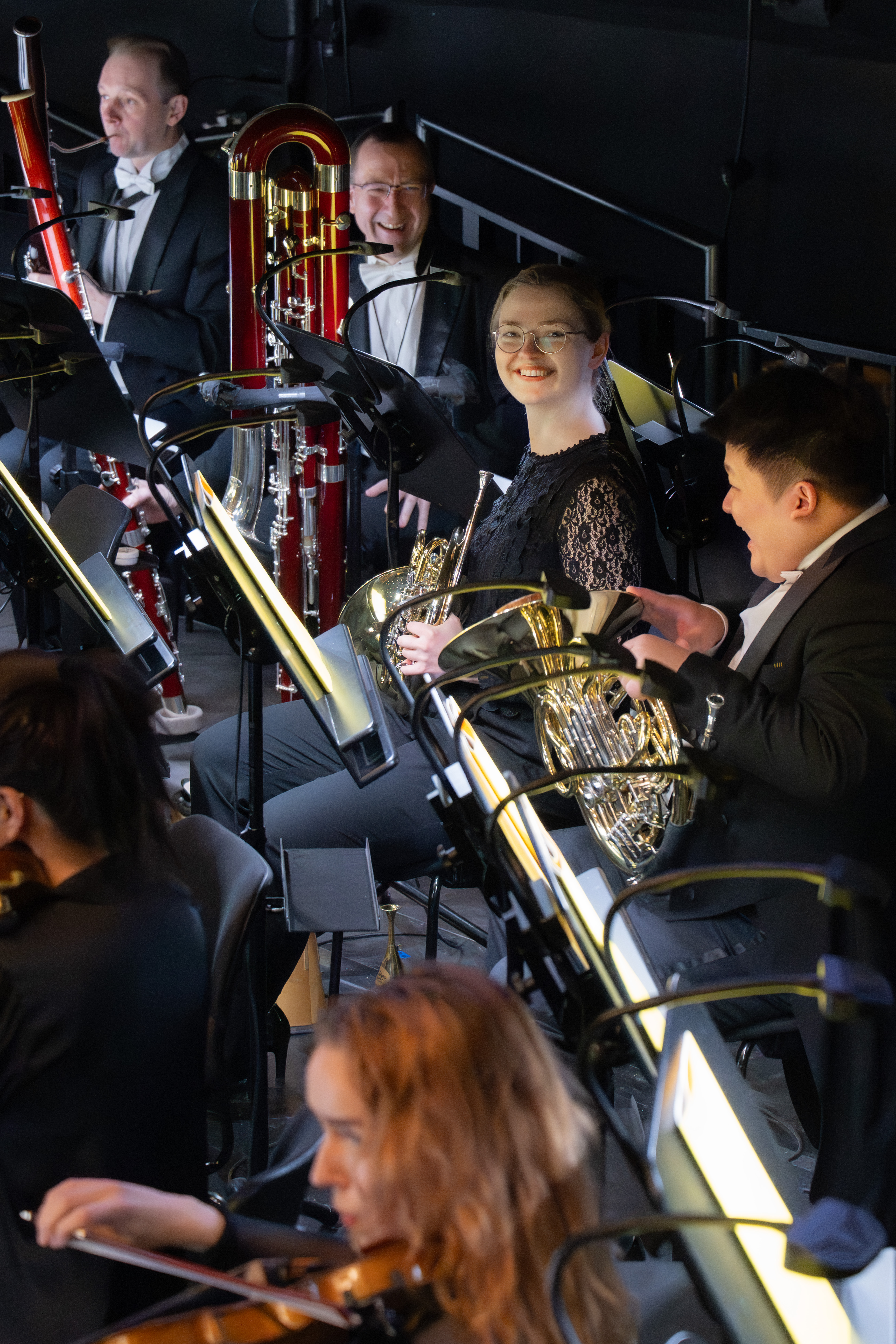 Orchestermusiker*innen in förmlicher Kleidung sitzen mit ihren Instrumenten, darunter Waldhörner. Hornistin Paula Ernesaks lächelt in die Kamera.
