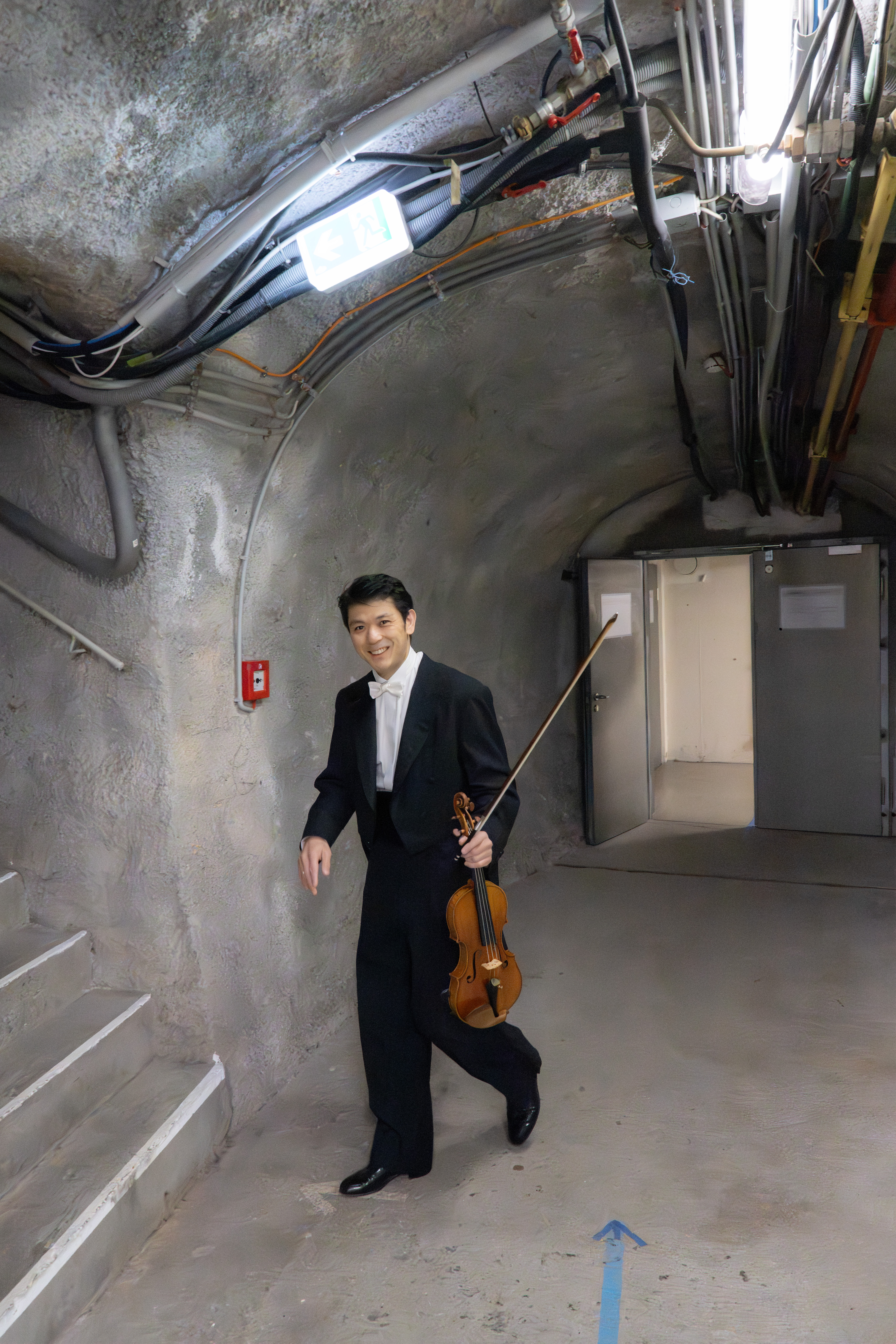 1. Konzertmeister Daishin Kashimoto mit seiner Geige in einem in Stein gemeißelten Tunnel auf dem Weg zum Orchestergraben in der Felsenreitschule.
