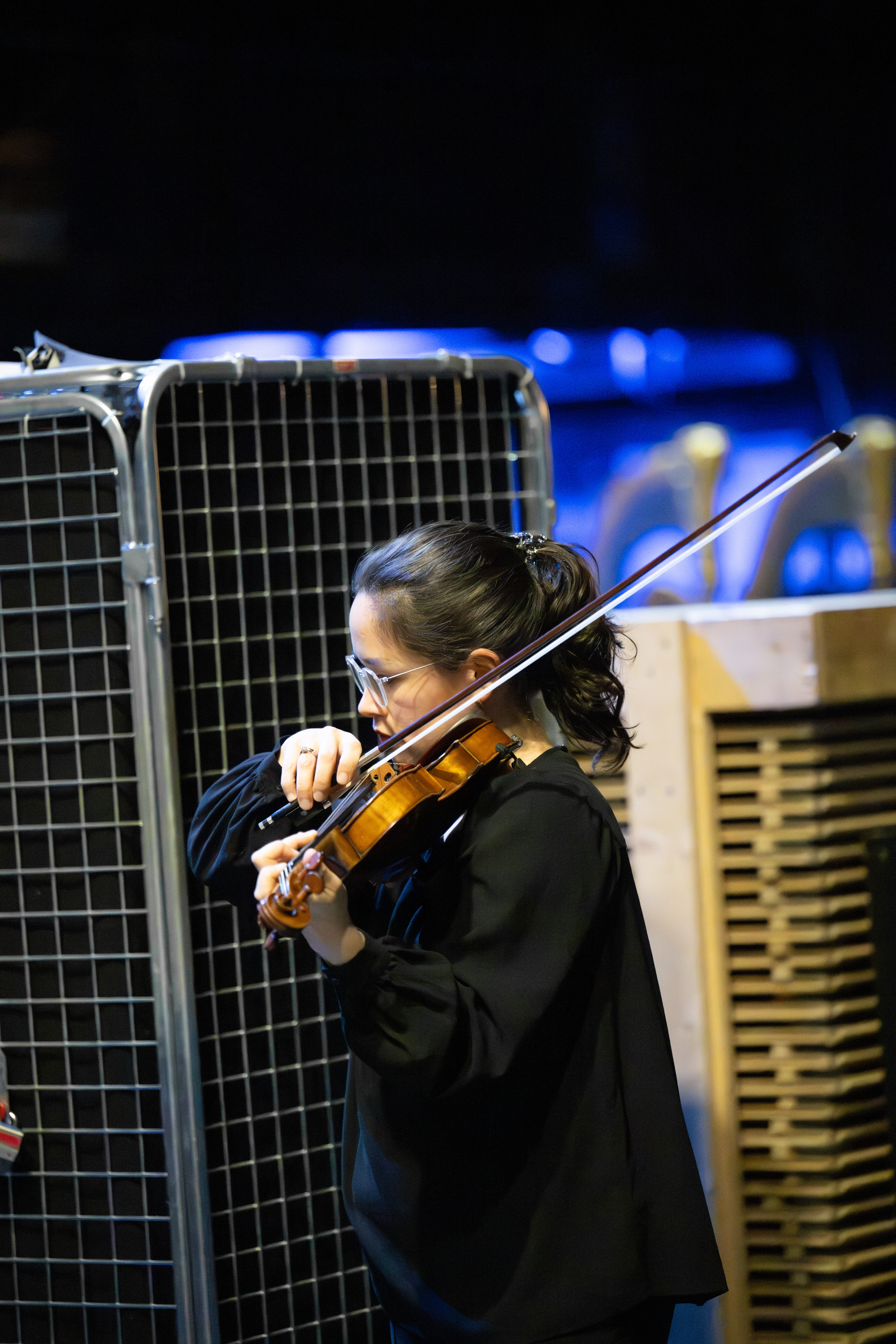 Eine schwarz gekleidete Frau spielt sich hinter der Bühne auf einer Geige ein.
