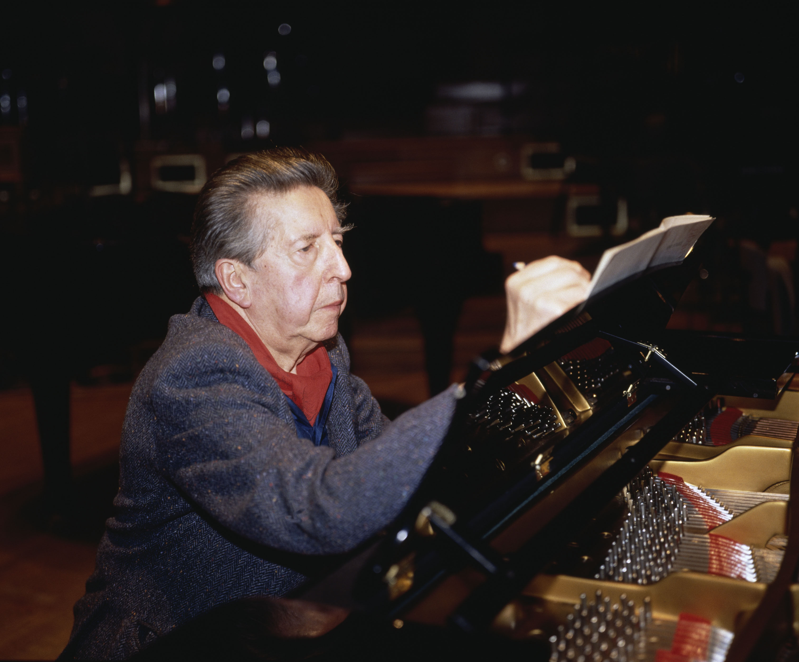 Henri Dutilleux is sitting at a piano and writing something down.