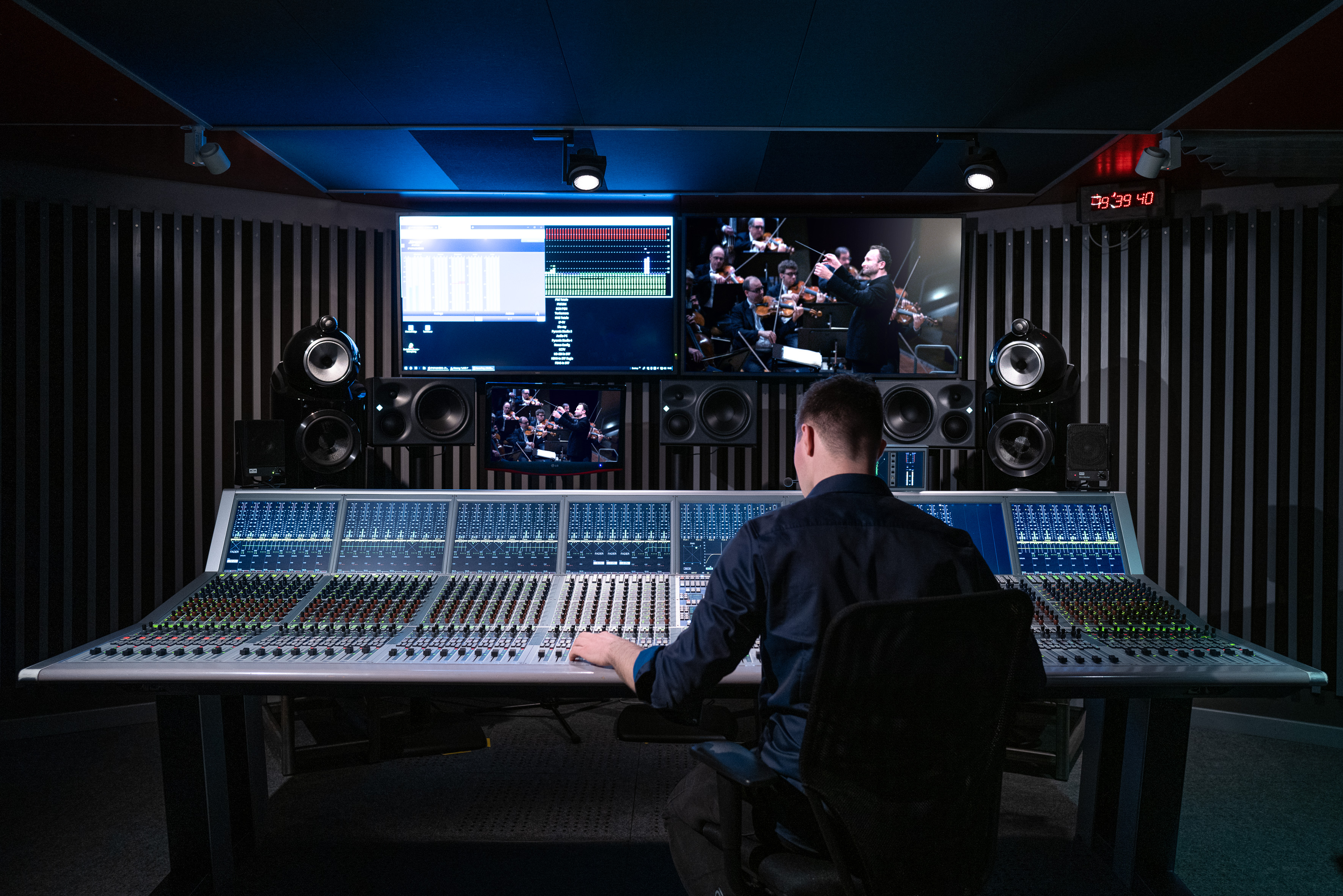 Ein Tonmeister sitzt vor einem Mischpult, im Hintergrund erkennt man Kirill Petrenko auf einem Bildschirm.