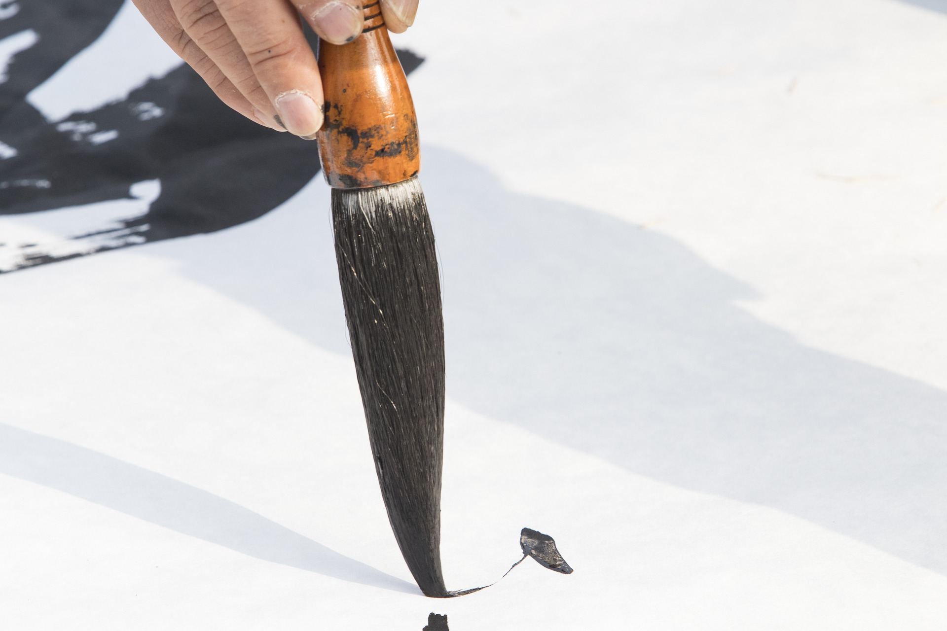 Eine Pinselspitze mit Tusche auf einem weißen Papier.