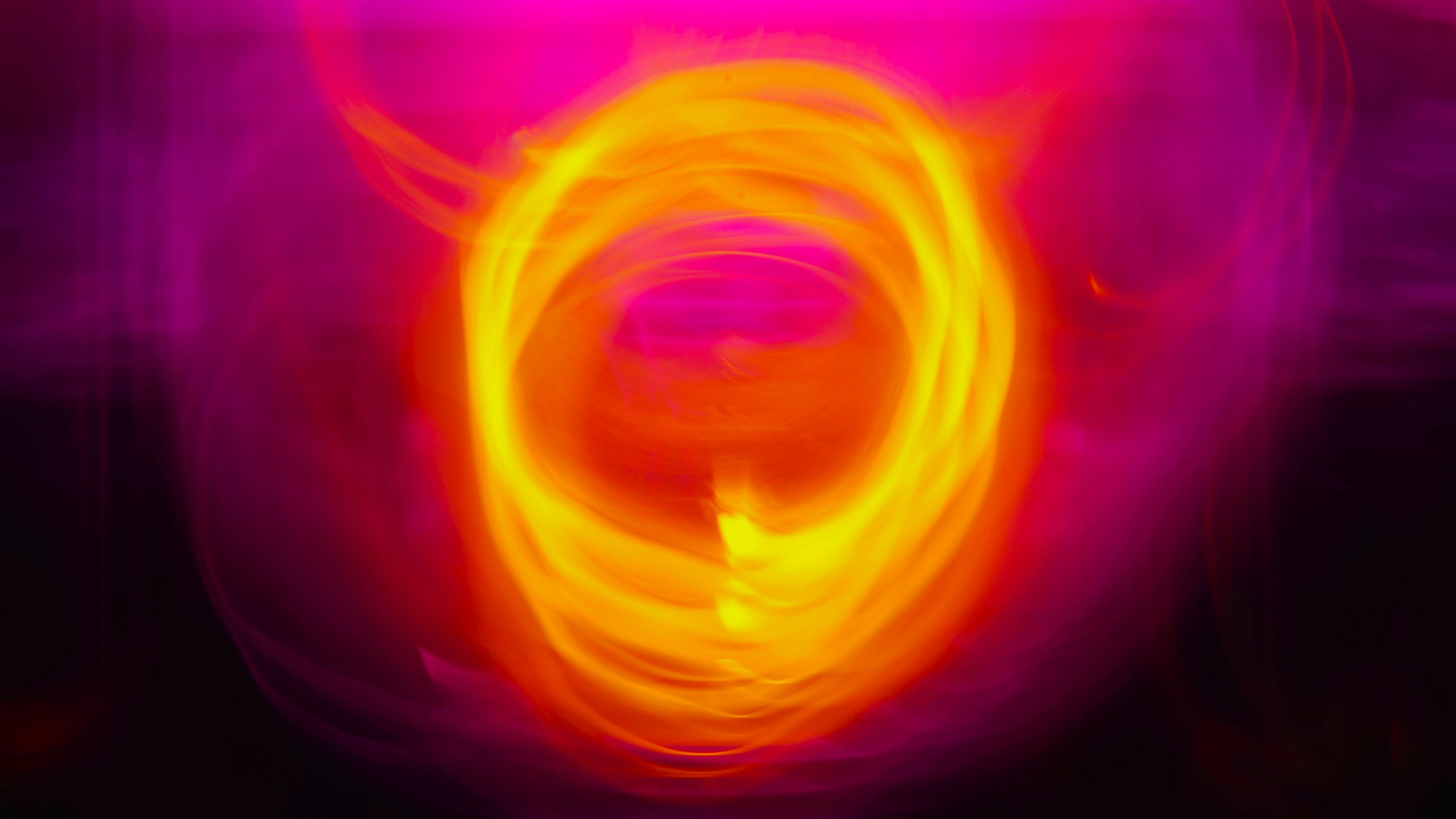 A swirling ring of bright yellow and orange light stands out against a soft, blurred pink and purple background, creating an abstract, fiery effect.