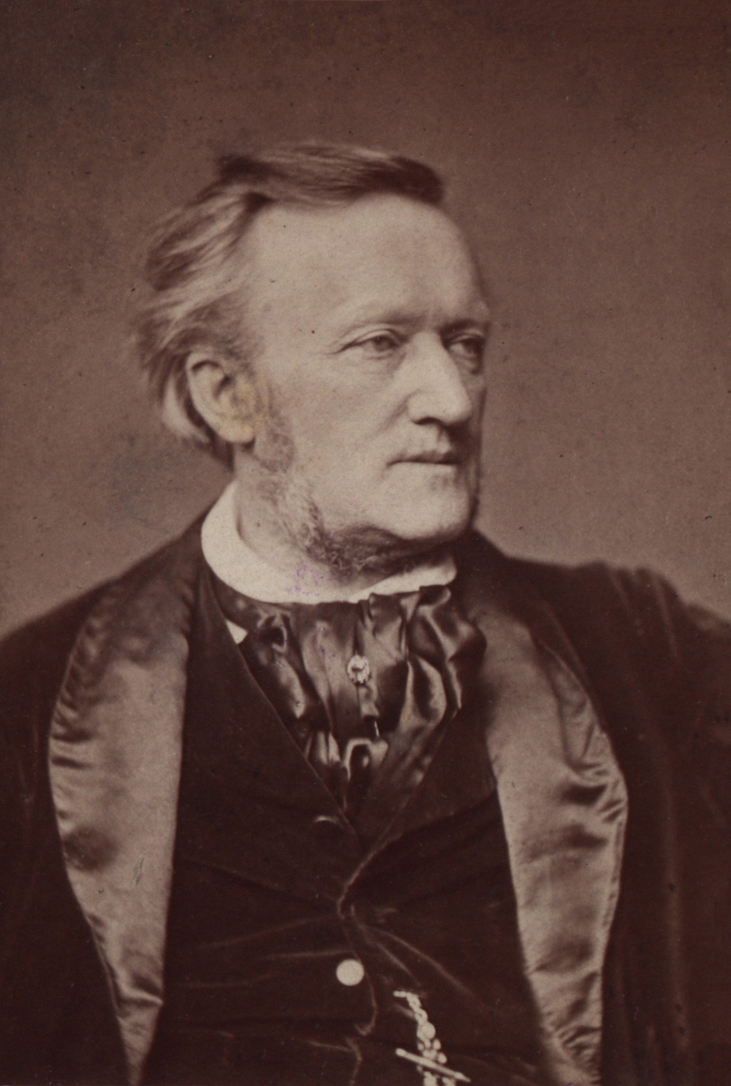 Sepia getöntes Porträt von Richard Wagner mit hellem Haar, Koteletten und ernstem Gesichtsausdruck, der eine dunkle Samtanzugsjacke und eine Krawatte trägt und leicht nach rechts blickt.