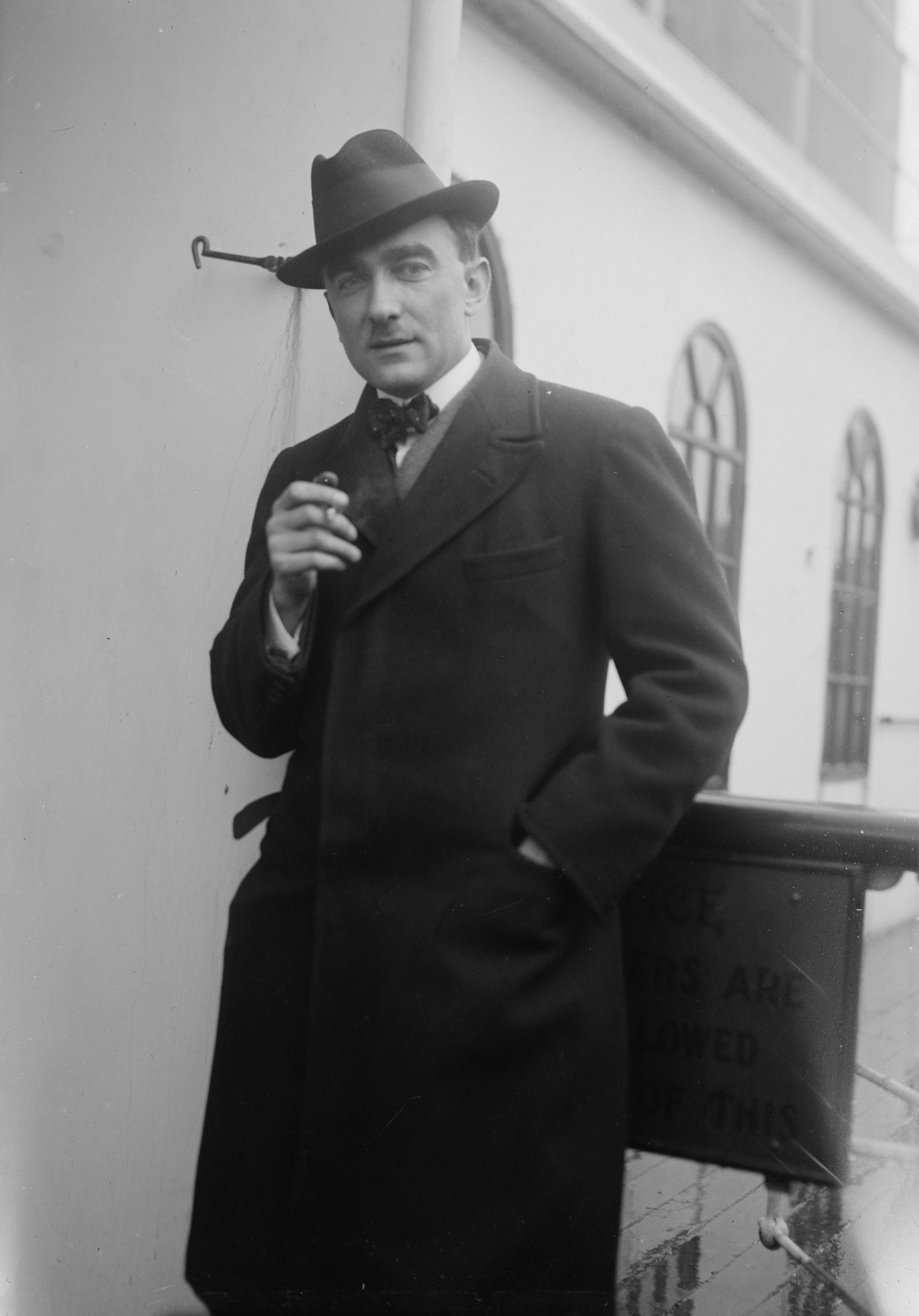 Porträt von Karol Szymanowski. Er trägt einen Mantel und einen Hut und hält eine Zigarette in seiner rechten Hand.