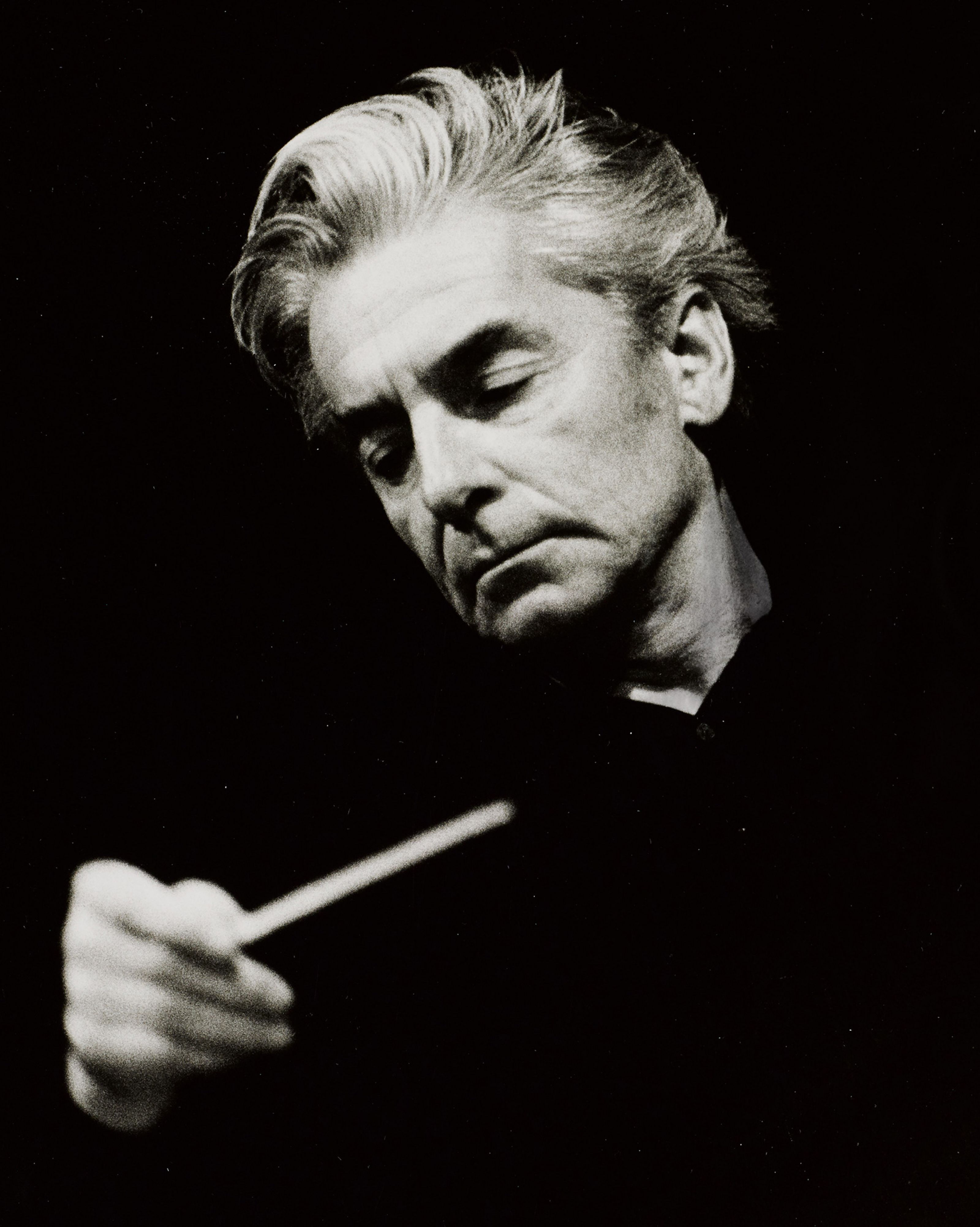 Herbert von Karajan, looking to his side, with his baton in his hands.