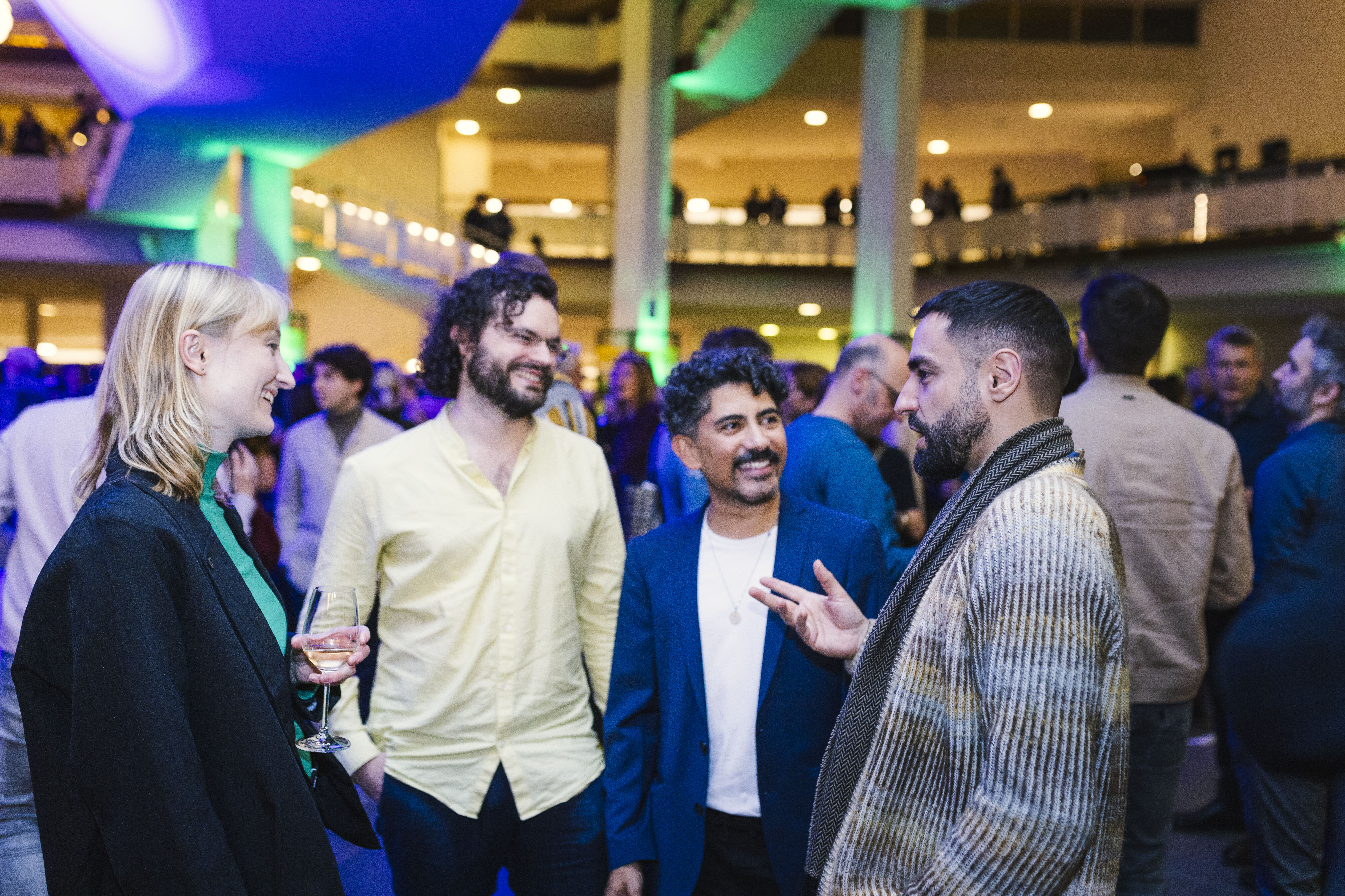 Vier junge Menschen stehen im Foyer der Philharmonie und reden miteinander. Sie lachen und haben offensichtlich eine gute Zeit. 